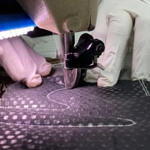 Industrial sewing machine stitching a shaped reinforcement pattern on a glove palm