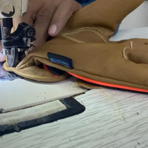 Operator stitching the reinforced cuff of a brown leather work glove